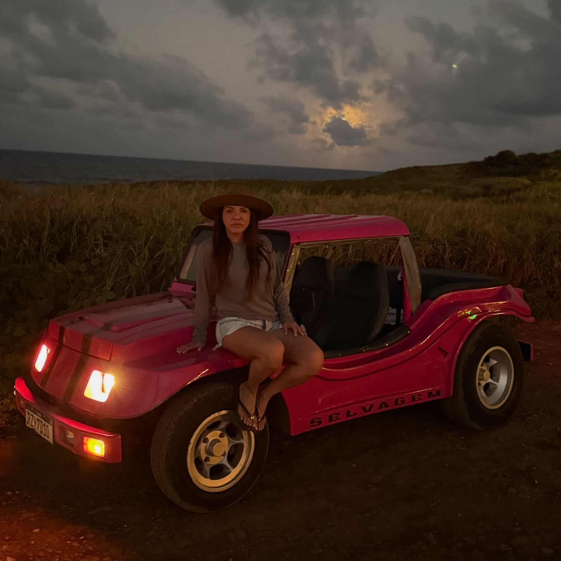 Mujer con sombrero sobre un buggy rosa al atardecer en Búzios